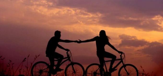Силуэт пары, держащейся за руки во время езды на велосипеде
