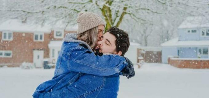 Мужчина несет женщину, которая целует его, пока идет снег.